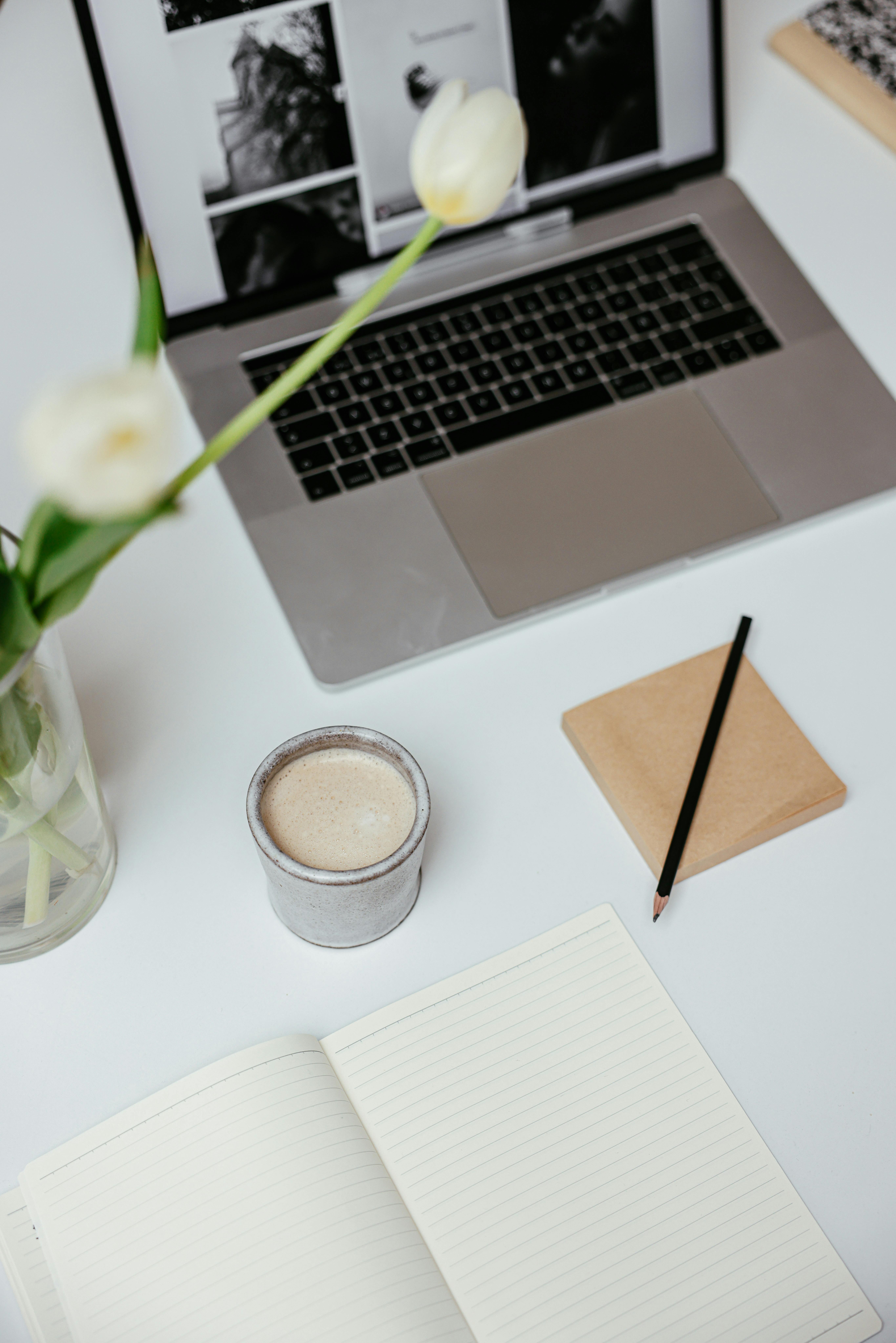 Workspace with laptop, tulips, coffee and notebook.